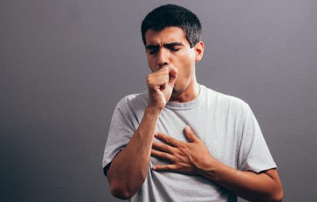 man coughing into fist and holding chest