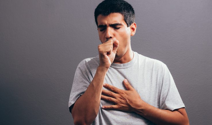 man coughing into fist and holding chest