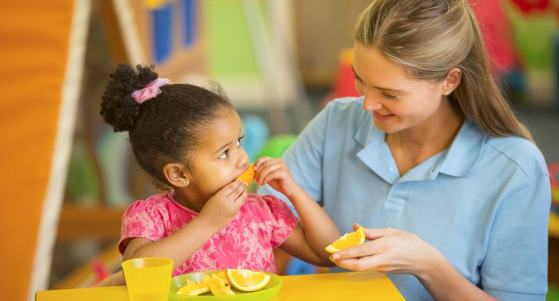 daycare teacher and young girl eating oranges