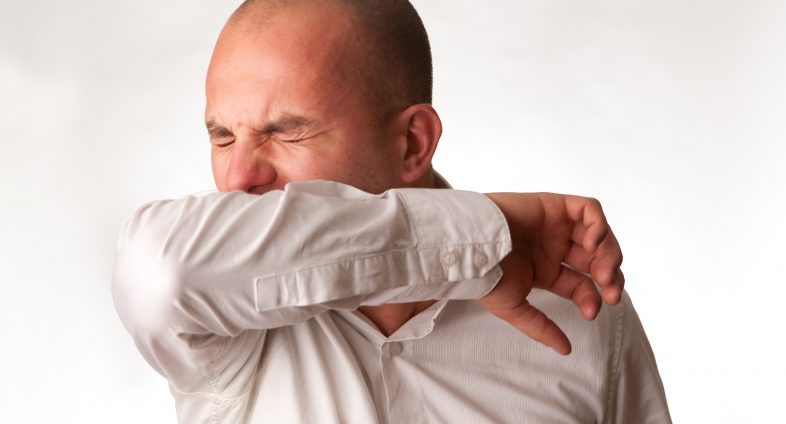 man sneezing into elbow