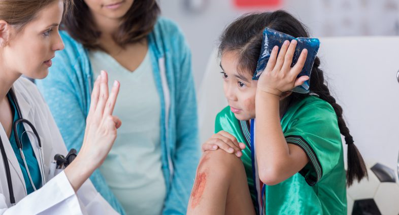 young girl holding ice pack to head being checked for concussion