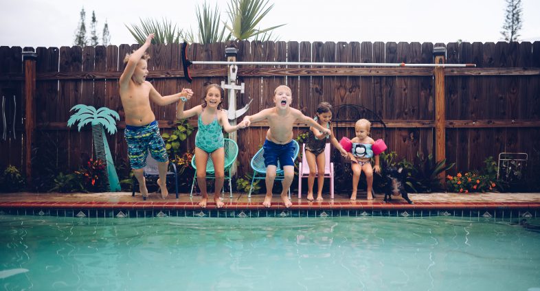 group of young kids jumping in backyard pool