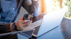 male hand holding smart phone in front of computer
